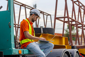 A male civil engineer in orange safety suit is using computer and application running a quality...