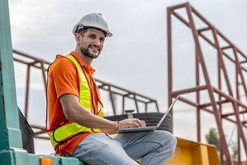 A male civil engineer in orange safety suit is using computer and application running a quality...