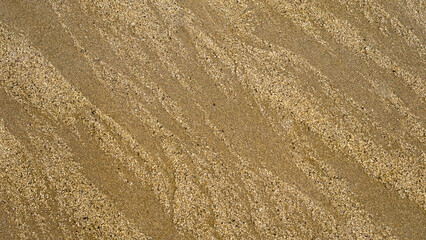 Diagonal close-up of textured beach sand with fine grains and natural wavy patterns. The intricate surface highlights the effects of wind and water erosion, creating a mesmerizing abstract design.