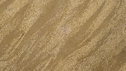 Close-up of beach sand with intricate wave-like textures formed by wind and water. The natural patterns create a visually appealing abstract background with fine grains and subtle color variations.