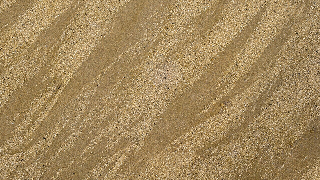 Close-up of beach sand with intricate wave-like textures formed by wind and water. The natural patterns create a visually appealing abstract background with fine grains and subtle color variations.
