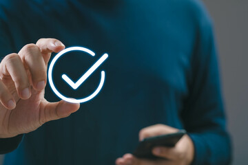 A person using a smartphone while holding a digital check mark symbol, representing confirmation,...