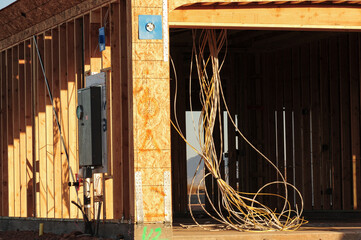 Exposed electrical conduit and service panel installed in a wood-framed house under construction,...