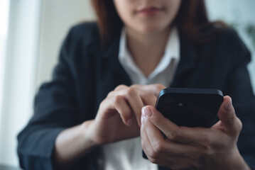 Close up of businesswoman using mobile smart phone during working on laptop computer at office. Asian business woman hand holding smartphone, connecting the internet