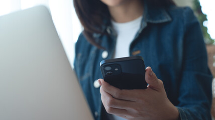 Asian business woman using mobile smart phone and online working on laptop computer, surfing the internet, searching the information at office, remote work, business casual, working at home concept