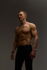 Fototapeta premium Slim muscular male model on black background. Shirtless fitness guy in black sweatpants posing in studio. Man with six pack abs in sunset light. Brutal photo