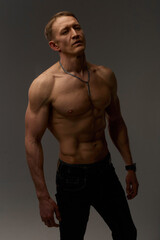 Fototapeta premium Slim muscular male model on black background. Shirtless fitness guy in black sweatpants posing in studio. Man with six pack abs in sunset light. Brutal photo