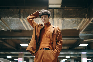 Stylish young man in a brown suit posing confidently in an indoor parking garage