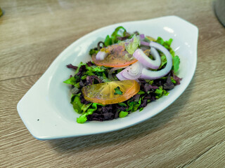 A white bowl with a salad of lettuce, tomatoes, and onions. The salad is served on a wooden table