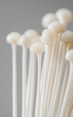 A close-up photograph of white enoki mushrooms against a light gray background, with blank space at the top and bottom for text. The composition is symmetrical, focusing on one side of the image. 