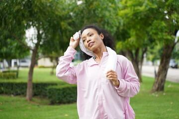 Fototapeta premium woman wiping sweat from face with towel after intense workout in relaxing green park