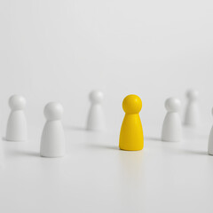 A yellow figure stands out among a group of white wooden figures on a white surface.
