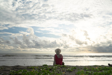 Fototapeta premium A woman sits alone and enjoys the view of the beach at sunset