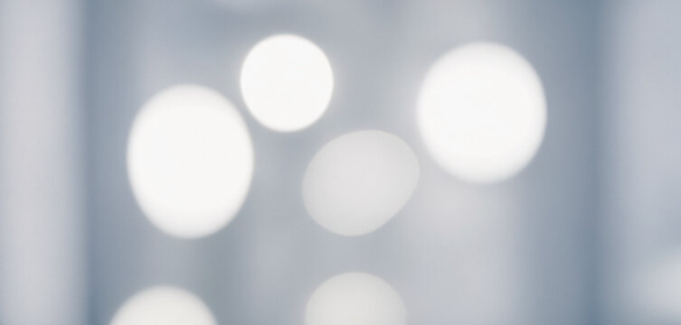Image shows an abstract background with several out of focus white light spots on a gray surface. Premium modern bokeh photos for poster, banner and print backgrounds.