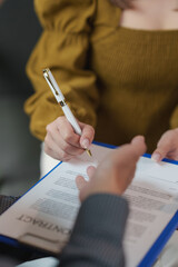 Businesswoman signing a contract on a clipboard, using an elegant white and gold pen, while a...