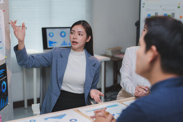 Businesswoman pointing at charts while explaining marketing strategies to colleagues during a meeting in a modern office, fostering collaboration and teamwork among the group