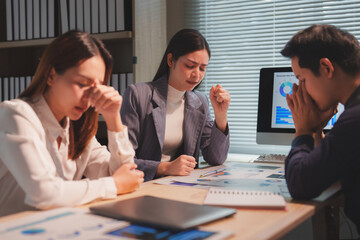 Asian businesspeople struggling with headaches and frustration while analyzing financial reports in an office, facing pressure and tight deadlines of corporate life