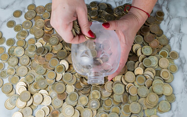 Woman's Hands Saving Money in Piggy Bank Amidst Colombian Coins: Financial Planning and Investment...