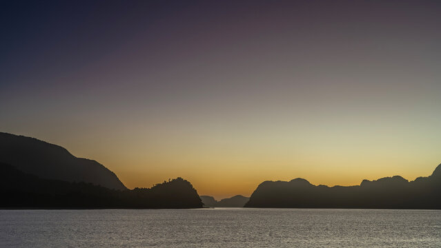 Evening twilight after sunset on a tropical island. The purple sky is highlighted with orange near the horizon. Silhouettes of mountains. Ripples on the surface of a calm ocean. Philippines. Palawan. 