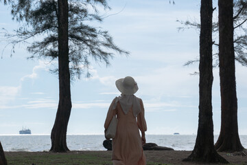 A woman walks alone on a tropical beach filled with tall pine trees