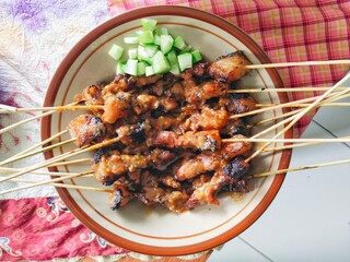 Indonesian beef satay on a plate on the table, served with pickled cucumber