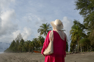 A woman walks through a row of coconut trees on a tropical beach in Indonesia