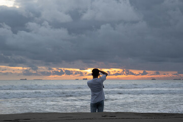 A man walks alone and takes pictures of the beach view at sunset