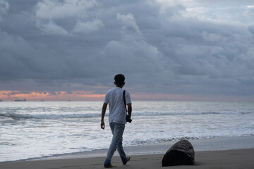 A man walks alone while carrying a camera and enjoying the view of the beach at sunset