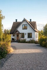 A delightful white house is nestled amid vibrant greenery, complemented by a charming gravel driveway, creating a picturesque landscape bathed in the warm glow of the golden hour