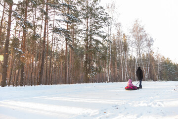 Dad takes his daughter on a snow tube in the forest