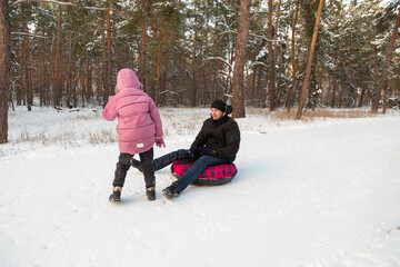 Father and daughter having fun with snow tube in the forest