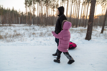 Dad with his daughter walking with snow tubing in the winter forest