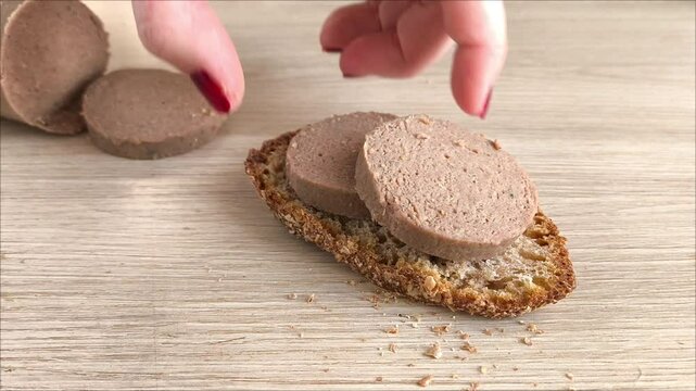 A woman makes a sandwich of liver sausage and rye bread. A woman's hand puts sausage slices on the bread. A sandwich made of dark bread. Pate.