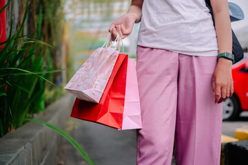 An Asian woman, is shopping in a stylish store during summer. She's holding several bags. 