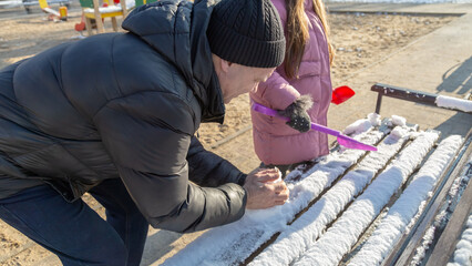 Grandfather with granddaughters making a little snowman in sunny winter day