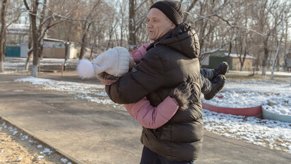 Grandfather playing with her granddaughter on the playground in the park in winter