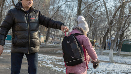 Grandfather walks with his granddaughter after school in the park in winter