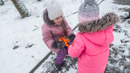 Two little girls in colorful clothes play outdoors during a snowfall.