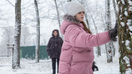Little girl in colorful clothes play outdoors during a snowfall.