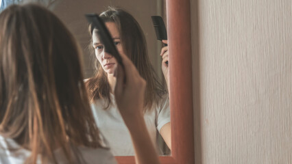 Young woman brushing hair brush looking at the mirror at bedroom