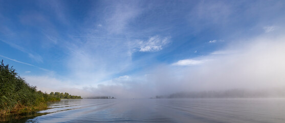 A foggy morning on a lake with a blue sky in the background