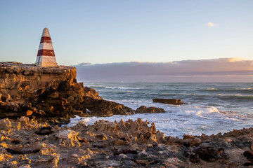 Historic Robe Obelisk stands tall on the rugged coastline of South Australia, surrounded by waves,...