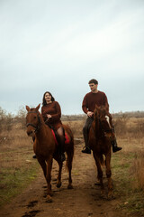 Naklejka premium Young romantic couple horse riding, against the background of a field with autumn grass
