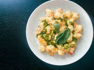 Gnocchi con ricotta e pesto Genovese, ricotta lemon sauce with thin ruffled carrots, Cherry tomatoes and basil on dark emerald green background, traditional Italian recipe, top down view