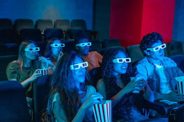 Young people wearing 3d glasses watching a movie and eating popcorn in a cinema