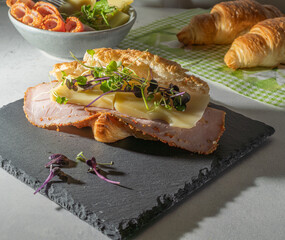 fresh golden croissant ham and cheese sandwich. sprout garnish. grey slate. morning sunlight. moody scene, close up, high angle view