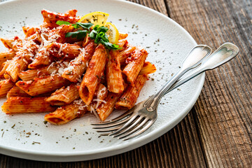 Penne noodles with tomato sauce and parmesan cheese served on wooden table	