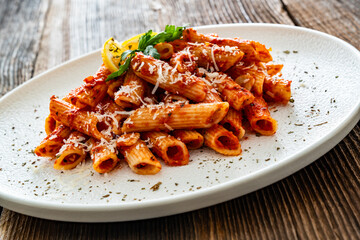 Penne noodles with tomato sauce and parmesan cheese served on wooden table	