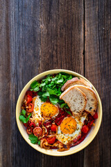Shakshuka - fried eggs with vegetables on wooden table	