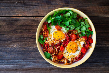 Shakshuka - fried eggs with vegetables on wooden table	